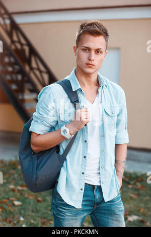 Junge stilvollen Mann in Jeans Kleidung mit einem Rucksack wandern im Hof Stockfoto