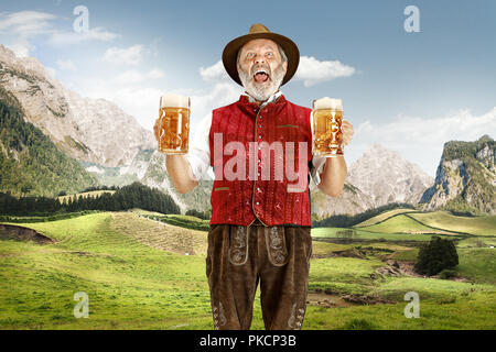 Deutschland, Bayern. Die senior glücklich singen Mann mit Bier im traditionellen österreichischen und bayerischen Kostüm gegen alpine Bergwelt angezogen. Oktoberfest, festival Konzept Stockfoto