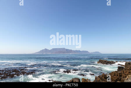 Kapstadt, Südafrika. Blick auf Table Mountain am Horizont, fotografiert von Robben Island, wo Nelson Mandela inhaftiert war. Felsen im Vordergrund. Stockfoto