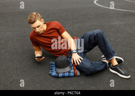 Moderne schöner Mann verwendet das Telefon und liegen auf dem Bürgersteig. Stockfoto