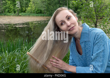 Schöne Frau Kämme langes Haar im Sommer Tag am Ufer des Flusses Stockfoto