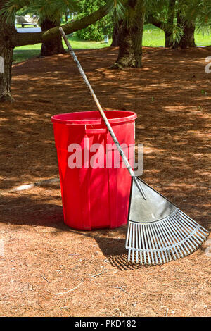 Aus rotem Kunststoff Mülleimer und Garten rake gegen sie lehnte sich während der Bereinigung der Hinterhof. Stockfoto