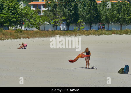 Zwei Touristen in einer Hängematte sitzen und ein anderes nicht ein Handtuch in der Wind am Strand von Portonovo, Galizien, Spanien, Stockfoto