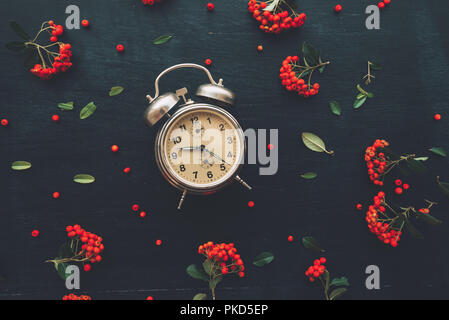 Flach vintage Wecker auf dunklen schwarzen Hintergrund, Ansicht von oben minimal Komposition mit retro Blumenschmuck Stockfoto