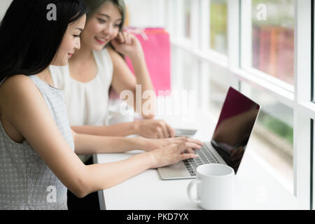 Zwei asiatische Frau zusammen Einkaufen mit Tüten in der Hand und mit Laptop, Shopping online Konzept. Stockfoto