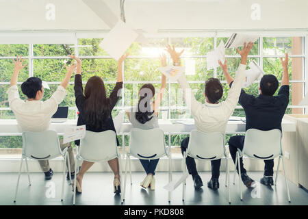 Erfolge feiern. Gruppe von jungen Geschäftsleuten Dokumente zu werfen und schauen glücklich beim Sitzen an ihren Arbeitsplätzen im Büro Stockfoto