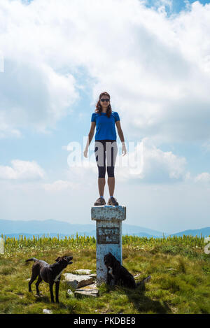 Stehendes Mädchen auf einem Peak Marker für ein Berg mit ihren beiden Hunden Stockfoto