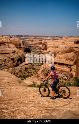 Eine Frau hält an der Blick hinunter eine Schlucht beim Reiten eines Mountainbike auf der weltberühmten Slickrock Trail in Moab, Utah, USA. Stockfoto