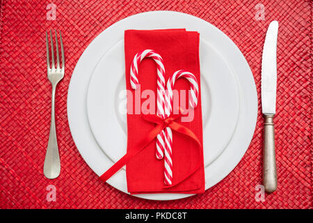 Weihnachten Tabelle einstellen. Zuckerstangen auf weißem Teller und Besteck, rote Matte, Ansicht von oben Stockfoto