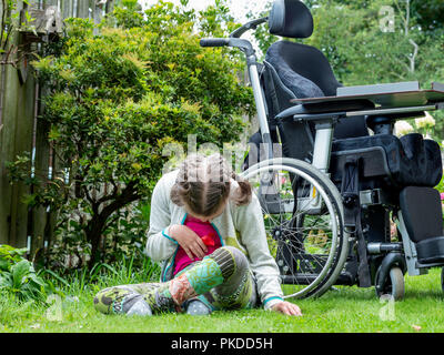 Ein behindertes Kind in eine Pause vom Sitzen in Ihrem Rollstuhl ihre natürliche Umgebung zu erkunden Stockfoto