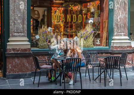 Zwei junge Frauen, die in einem Café in Galerien Royales Saint Hubert, Brüssel Sitzung, wobei Souvenir selfie Fotografien, Brüssel, Belgien Stockfoto