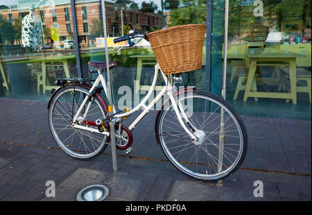 Eine weiße Damen Fahrrad mit einem niederländischen Stil open frame hintere Träger und einen Korb auf den Griff Bars außerhalb einer Kunstgalerie gesperrt Stockfoto