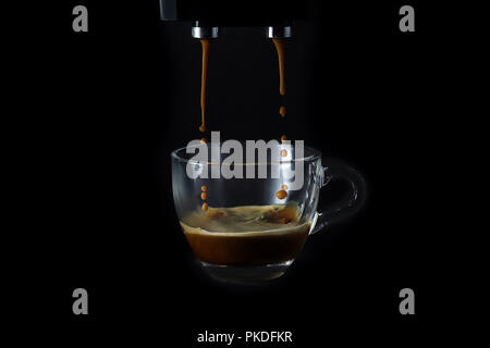 Tasse Espresso während Füllen in einer Kaffeemaschine, auf schwarzem Hintergrund, splash, noch Leben. Stockfoto