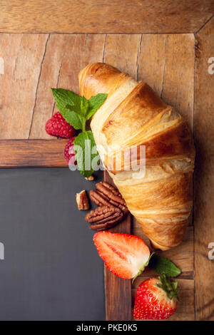 Schwarze Schiefertafel mit Croissant und Beeren Stockfoto