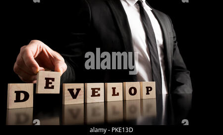 Nahaufnahme, Geschäftsmann arrangieren kleine Holzteile mit entwickeln Buchstaben auf schwarzem Hintergrund. Stockfoto