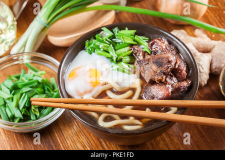 Japanische Udon Nudeln mit Rindfleisch, Ei, grüne Zwiebeln und Suppe in eine braune Schale Stockfoto