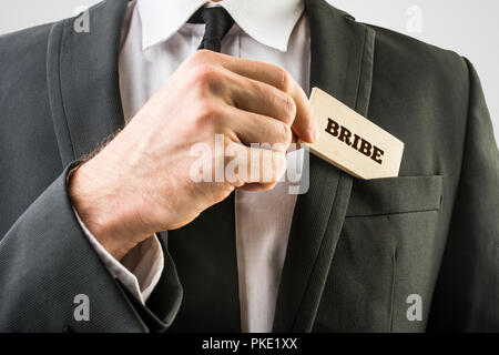 Einfache Bestechung Konzept - Nahaufnahme, Geschäftsmann, der in schwarzen Anzug, kleine Holz- Stück mit Schmiergeld Text vor Anzug Tasche. Stockfoto