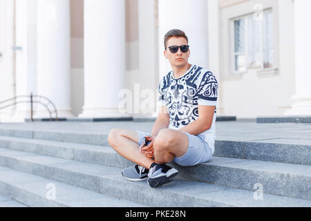 Junge stilvoll trendy Mann in Sonnenbrille sitzen auf der Treppe. Stockfoto