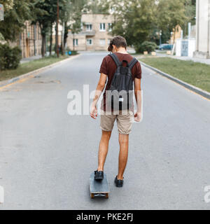 Junger hübscher Kerl mit einem Rucksack, ein Skateboard auf der Straße Stockfoto