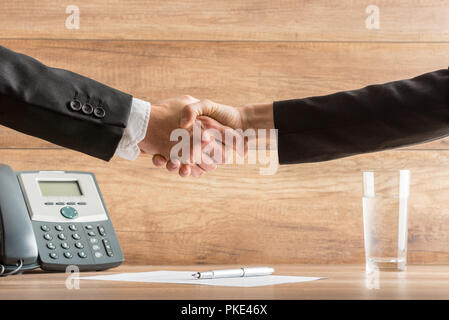 Handshake der beiden Geschäftspartner nach einem erfolgreichen Meeting im Büro, oben einen Vertrag unterschrieben, auf hölzernen Schreibtisch platziert, in der Nähe des Telefon. Stockfoto