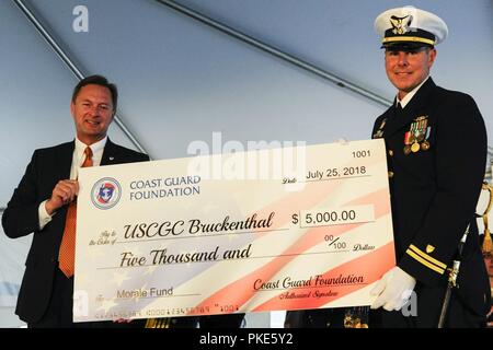 Robert Montgomery, Verwalter der Coast Guard Foundation, präsentiert ein prüfen, Oberstleutnant Bryan Kilcoin, kommandierender Offizier der Coast Guard Cutter Nathan Bruckenthal, bei der Inbetriebnahme des Schiffes Zeremonie in Alexandria, Virginia, 25. Juli 2018. Die Überprüfung wurde für die Moral Fonds des Werkzeugs vorgestellt. Stockfoto