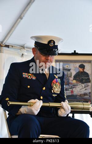 Chief Petty Officer Joseph Ruggiero blickt auf eine lange, während die Symbolik der seine Bedeutung während der Inbetriebnahme Zeremonie für das Patrouillenboot Bruckenthal in Old Town Alexandria, Virginia, 25. Juli 2018 dem Publikum gelesen wird. Ruggiero wurde auf die USS Feuerblitz mit Petty Officer 3rd Class Nathan Bruckenthal, der tödlich während der Operation Iraqi Freedom im Arabischen Golf im Jahr 2004 verwundet wurde zugewiesen. Us-Küstenwache Stockfoto