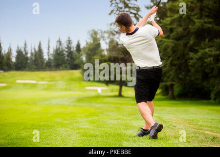 Ein männlicher Golfspieler driving a Golf Ball hinunter die Fahrrinne eines Golfkurses mit der Kugel in der Luft; Edmonton, Alberta, Kanada Stockfoto