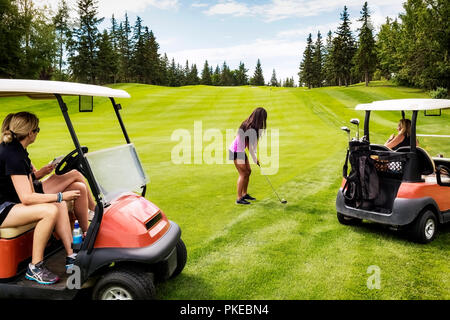 Eine Gruppe von weiblichen Golfern beobachten von ihren Golfwagen, während ihre Mitspieler plant ihr Schuss aus dem rauen auf einem Golfplatz auf einem warmen Summ... Stockfoto