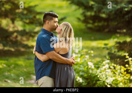 Ein gemischtes Rennen Ehepaar Stoppen in einem Stadtpark zu küssen, während sie Zeit gemeinsam an einem warmen, sonnigen Nachmittag genießen; Edmonton, Alberta, Kanada Stockfoto