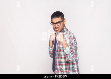 Wütend bärtigen Geschäftsmann in bunt kariertem Hemd, blaue Krawatte und schwarze Brillen stehen und von der Kamera mit aggressiven Gesicht und Faust. ind Stockfoto