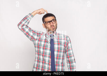 Portrait von nachdenklich aussehenden bärtigen Geschäftsmann in bunt kariertem Hemd, blaue Krawatte und Brille stehen und weg schauen mit lustigen Gesicht. Stockfoto