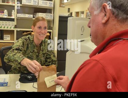 JACKSONVILLE, Fla. (27 Juli 2018) Hospital Corpsman 2. Klasse Jamie Hopkins liefert Medikamente zu Terry Thornhill am Naval Hospital Jacksonville Apotheke. Das Krankenhaus ist die Einführung einer verbesserten Prozess für die Patienten die Medikamente in der Krankenhausapotheke und Sat-Apotheke abholen, in der ab Anfang August. Die Apotheke Check-in Kiosk ermöglicht es Patienten, die durchschnittliche Wartezeit zu sehen, und melden Sie sich Textnachrichten mit Aktualisierungen über den Status ihrer Verschreibung zu erhalten. Stockfoto