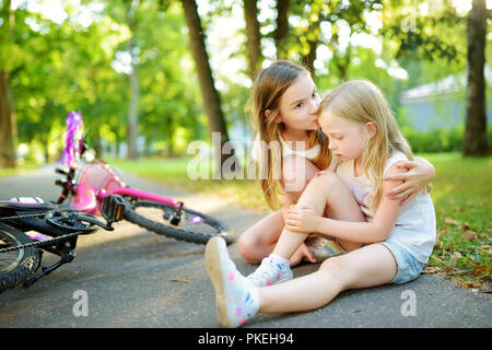 Adorable Mädchen tröstend ihre kleine Schwester, nachdem Sie weg fiel ihr Fahrrad im Park. Kind verletzt, während auf einem Fahrrad. Aktive Familie leisur Stockfoto