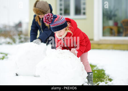 Adorable kleinen Mädchen einen Schneemann bauen im Hinterhof. Süße Kinder spielen im Schnee. Winter Aktivitäten für Kinder. Stockfoto