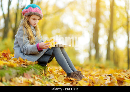 Süße kleine Mädchen Skizzieren auf schönen Herbsttag. Glückliches Kind spielen im Herbst Park. Kid Zeichnung mit Bunte Bleistifte. Herbst Aktivitäten Stockfoto