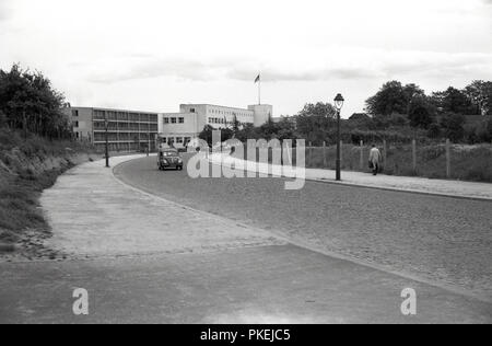 1950, historische, Nachkriegszeit, Koln, Deutschland, ein Volkswagen Immobilien Auto auf einer Straße mit Kopfsteinpflaster mit modernen Gebäude im Hintergrund. Stockfoto