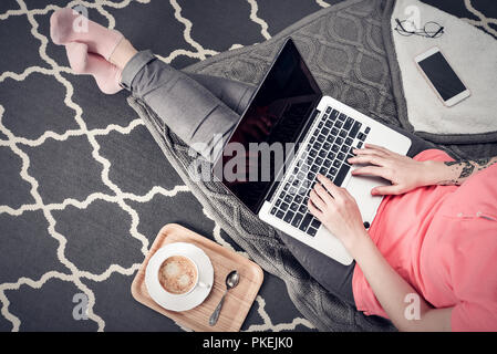 Junge kreative Frau auf dem Boden sitzen und arbeiten mit Laptop, Tasse Kaffee und Handy, Ansicht von oben Stockfoto