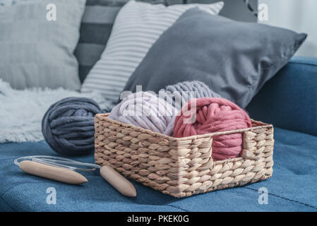 Kugeln von Super chunky Merino Wollgarn mit Nadeln im rustikalen Korb auf Auf flauschigen weissen Fell Hintergrund. Stockfoto