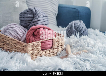 Kugeln von Super chunky Merino Wollgarn mit Nadeln im rustikalen Korb auf Auf flauschigen weissen Fell Hintergrund. Stockfoto
