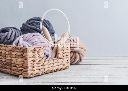 Kugeln von Super chunky Merino Wollgarn mit Nadeln im rustikalen Korb auf hellblauem Hintergrund. Stockfoto