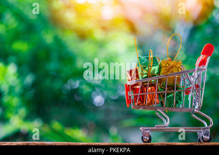 Trolley für Supermarkt oder Warenkorb und Geschenkboxen mit grünen Natur Hintergrund. Geschenke zu kaufen. Stockfoto
