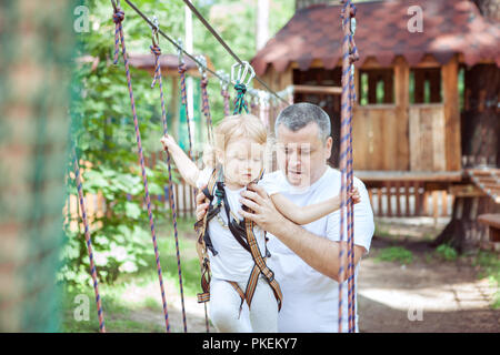 Junger Vater hilft, seine Tochter, die Hindernisse im Hochseilgarten überwinden. Stockfoto