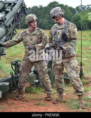 Sergeant Lucas Frazee informiert ausgehende im Field Artillery Kommandeur, Oberstleutnant Joseph Rhees, auf, wie man Feuer die M777A2 155mm Howitzer während einer Live Fire Training am Fort Chaffee gemeinsame Manöver Training Center, 28. Juli 2018 gezogen. Stockfoto