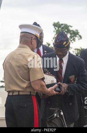 Ehemalige US Marine Corps Sgt. John Spencer (rechts), präsentiert Generalleutnant Robert Hedelund, Kommandierender General, II Marine Expeditionary Force, mit einem Geschenk während der montford Punkt Gifting Zeremonie an Lejeune Memorial Garden in Jacksonville, N.C., am 25. Juli. Der Zweck der Zeremonie wurde offiziell in Besitz der Nationalen Montford Point Marine Denkmal für die Abteilung der Marine übertragen. Stockfoto