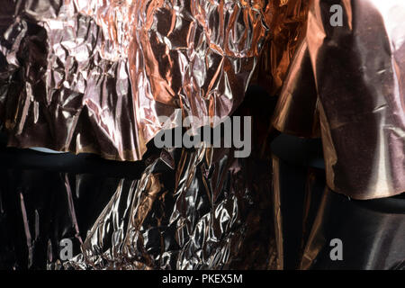 Metallisch glänzenden gold bronze Alufolie auf einem schwarz glänzenden Oberfläche spiegelt zerquetscht. Zerknitterte Blatt unebenen Folie. Stockfoto