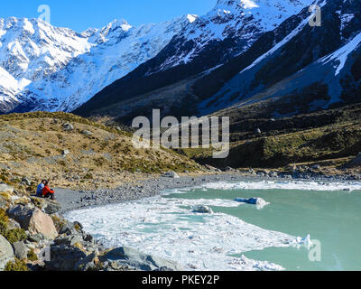 Zwei Personen genießen Sie die atemberaubende Aussicht auf die Gletscher Tasman See in Aoraki Mount Cook Nationalpark. Weiße schneebedeckte Berge, felsige Vordergrund Stockfoto