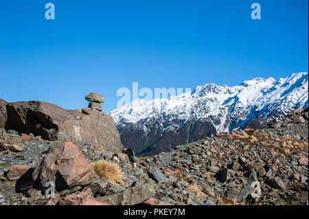 Ein Felsen Cairn hebt sich von einem tiefblauen Himmel in einem verschneiten Berglandschaft. Wanderweg im Hooker Valley führt zu Aoraki Mount Cook, Stockfoto