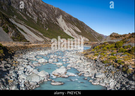 Gletscherbach im Hooker Valley, Aoraki Mount Cook Nationalpark. Aqua River fließt durch felsige Landschaft, Geröllhalden und blauer Himmel Hintergrund Stockfoto