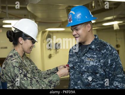 NEWPORT NEWS, Virginia (Aug. 3, 2018) das Schiff Veteran 2. Klasse Derek Lindberg, aus Manila, Philippinen, USS Gerald R. Ford's (CVN 78) Versorgung der Abteilung zugewiesen, erhält seine gute Führung Medaille vom Master Chief Logistikspezialisten Jeany Nemenzo während einer Auszeichnungen bei Viertel Zeremonie in der Waffen handling Bereich onboard Ford. Stockfoto