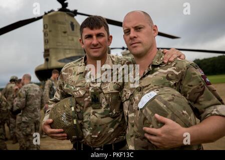 Warrant Officer I Biggs und Sgt. Ross Hastie aus dem 16 Air Assault Brigade HQ, Vereinigtes Königreich, posieren vor einem US Army CH-47 Chinook Hubschrauber nach anhaltendem Airborne Training während der Leapfest an der Universität von Rhode Island, West Kingston, R.I., Aug 4, 2018. Leapfest ist der größte und am längsten bestehende, internationale statische Linie Fallschirm Training und Wettbewerb veranstaltet vom 56. Truppe den Befehl, Rhode-Island Army National Guard hohen Niveau zu fördern technische und Korpsgeist innerhalb der internationalen Gemeinschaft in der Luft. Stockfoto